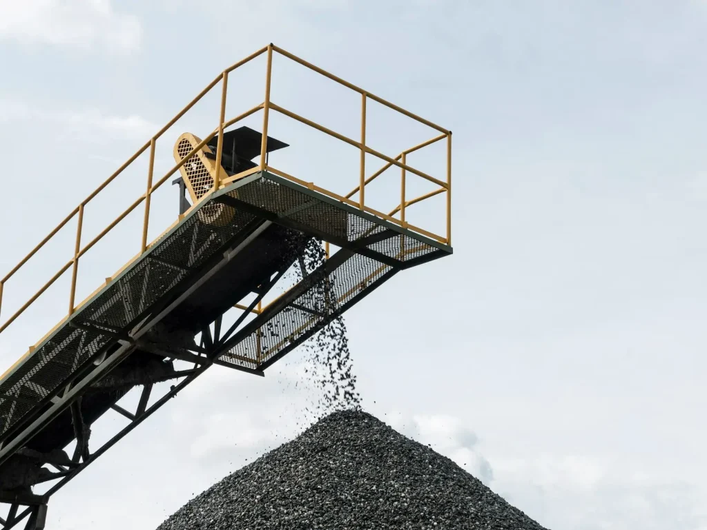 Crushed stone falling from a conveyor onto a conical stockpile of graded aggregate