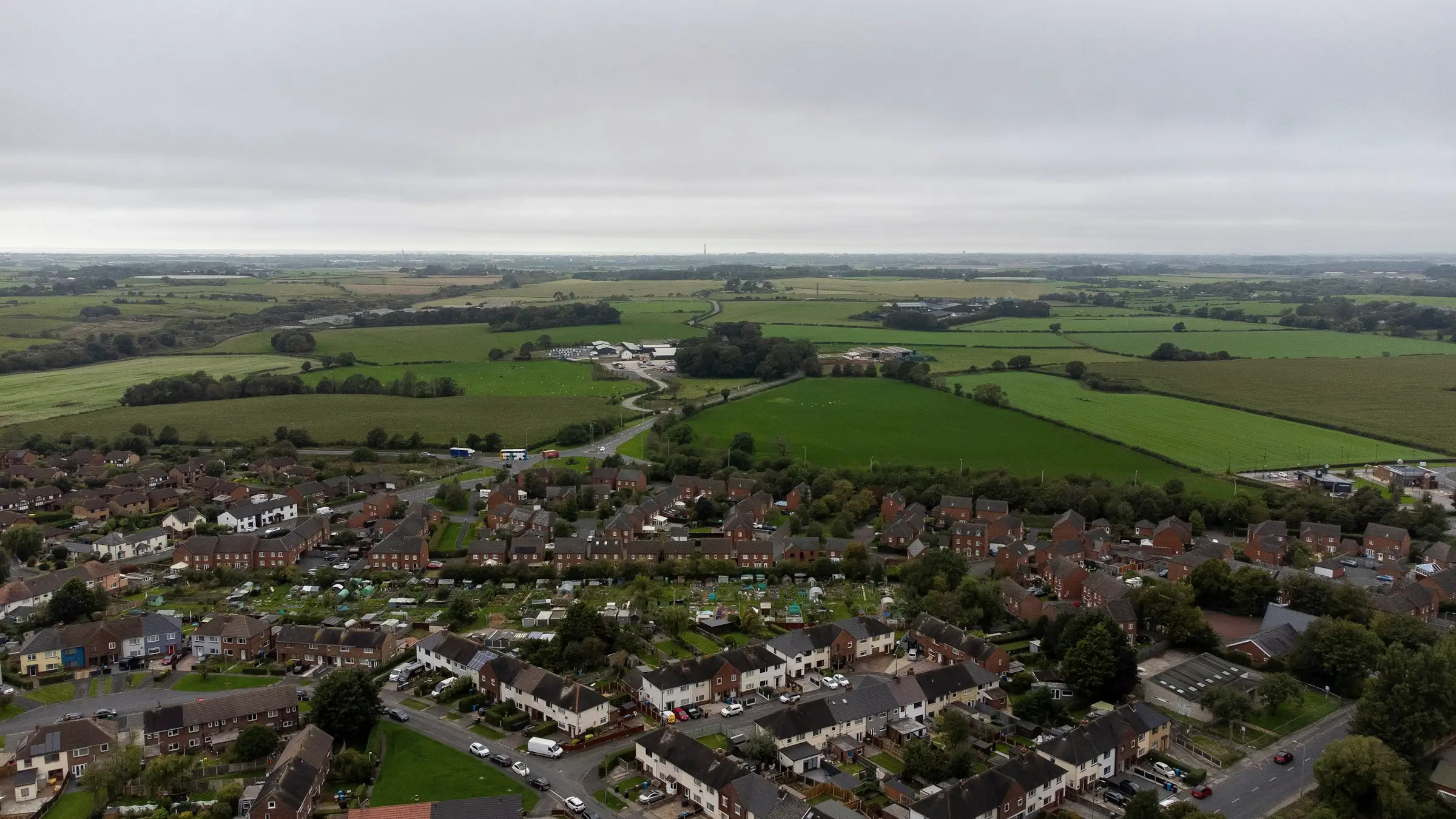 Aerial view of a town of brick houses bordered by green fields under an overcast sky