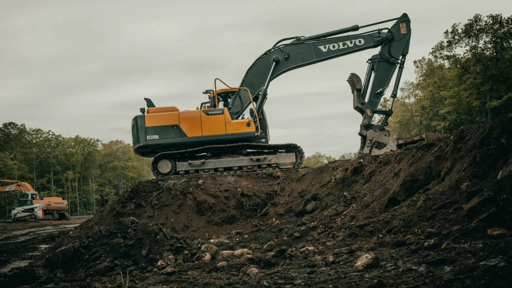 A tracked excavator working on top of a mound of excavated earth at the edge of a cleared site
