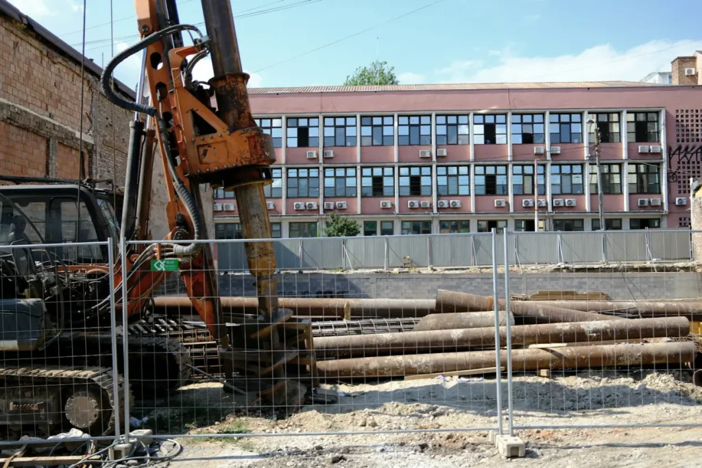 A bored-piling rig and steel casings on a fenced construction site