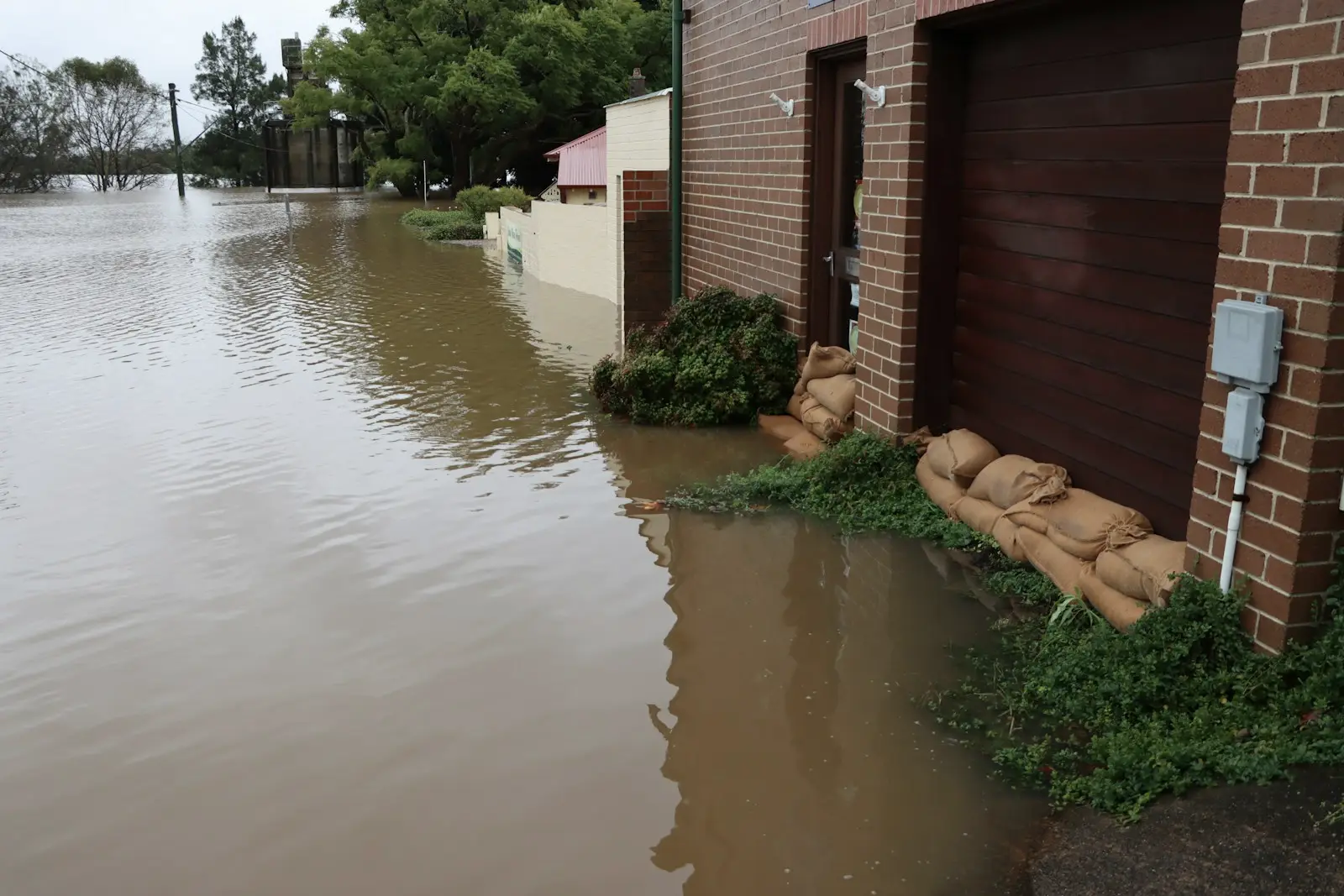 Sandbags stacked against a brick garage door as flood water covers a residential street