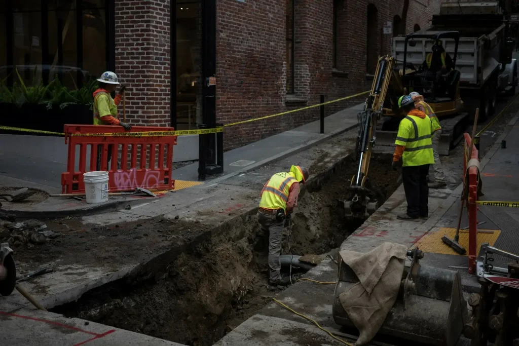 Operatives in hi-vis working in a service trench excavated along a town street, with barriers around the works